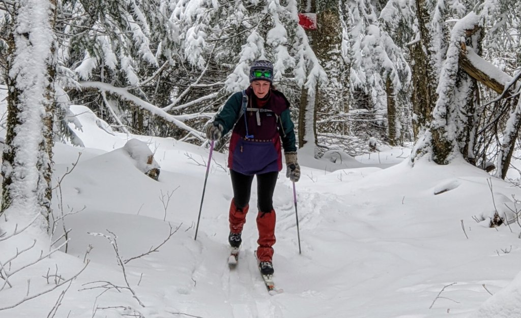 A skier skins up a forested trail