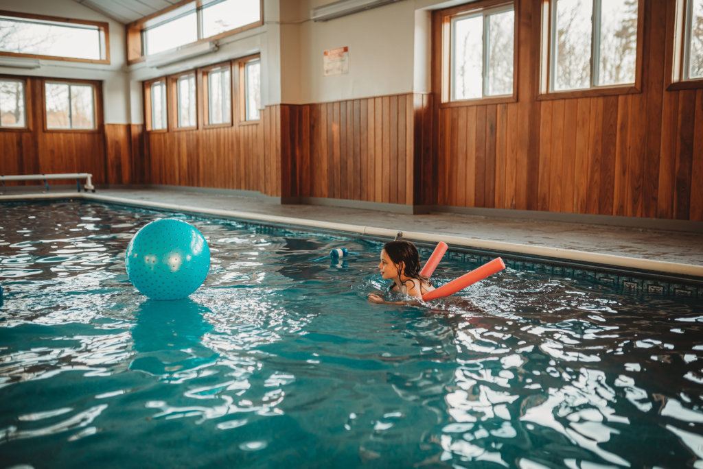 Child floats on a pool noodle at the indoor pool