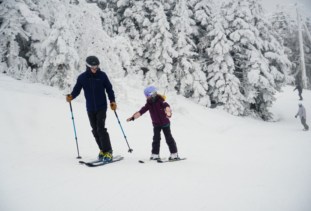 Snowy mountain trail with a parent and child skiing down together