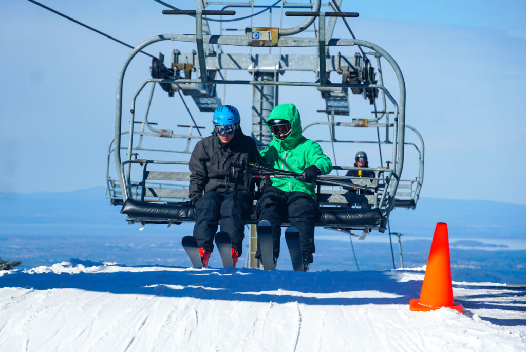 VT Adaptive volunteer and skier prepare to offload the ski lift with mountain views in the background