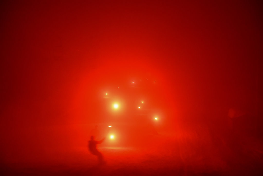 Blurry shot of a snowboarder riding down the slope with red flares in the distance from the torch light parade